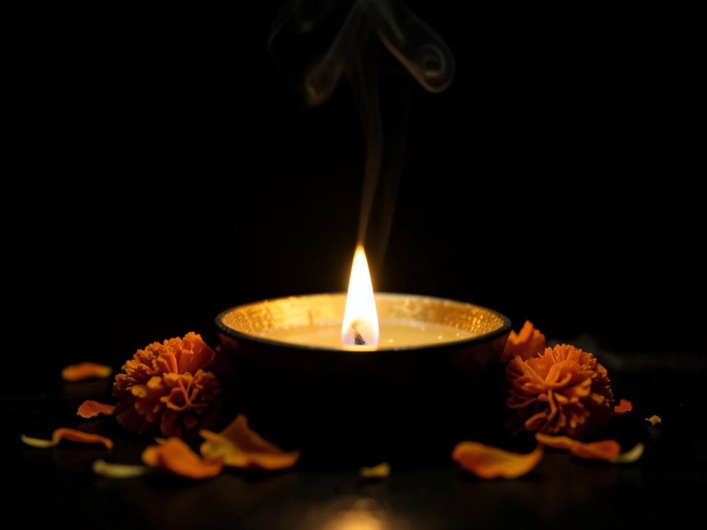 A single lit diya lamp surrounded by marigold petals in darkness